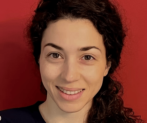 Eine Frau mit lockigen dunklen Haaren lächelt vor einem leuchtend roten Hintergrund und trägt ein dunkles Oberteil Eine Frau mit lockigen dunklen Haaren lächelt vor einem leuchtend roten Hintergrund und trägt ein dunkles Oberteil