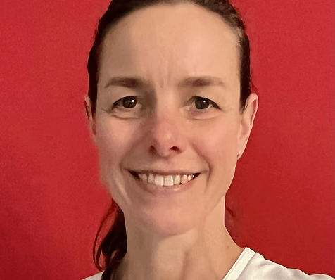 Eine Frau mit braunen, zurückgebundenen Haaren lächelt und trägt ein weißes Oberteil vor einem leuchtend roten Hintergrund Eine Frau mit braunen, zurückgebundenen Haaren lächelt und trägt ein weißes Oberteil vor einem leuchtend roten Hintergrund
