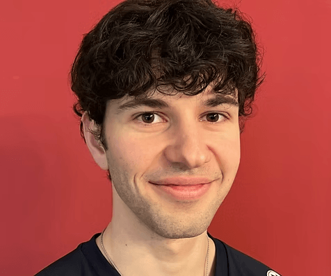 Ein junger Mann mit lockigen dunklen Haaren lächelt vor einem einfarbigen roten Hintergrund Ein junger Mann mit lockigen dunklen Haaren lächelt vor einem einfarbigen roten Hintergrund